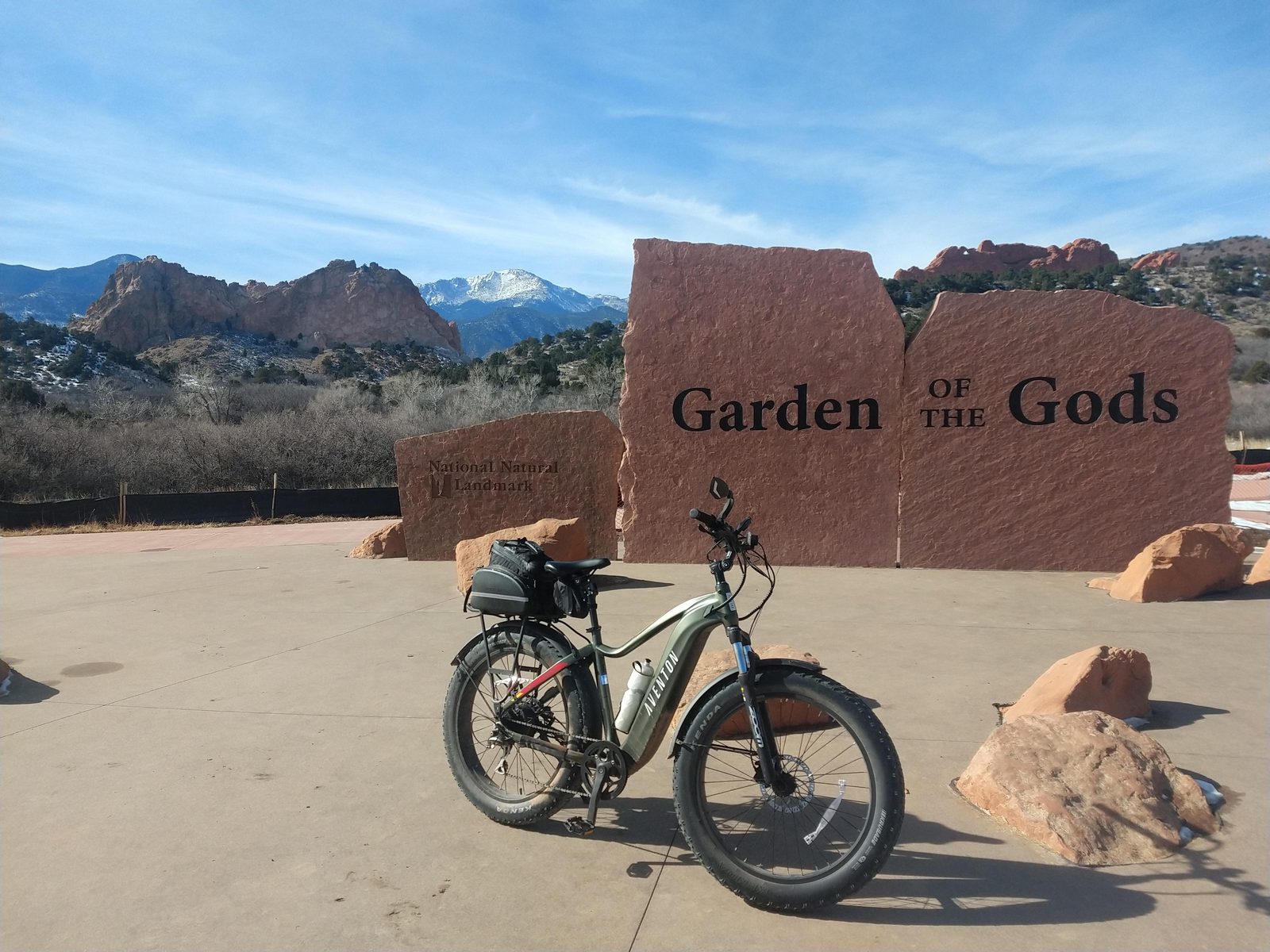 Dom's e-bike parked at a Garden of the Gods entrance sign with Pikes Peak behind it